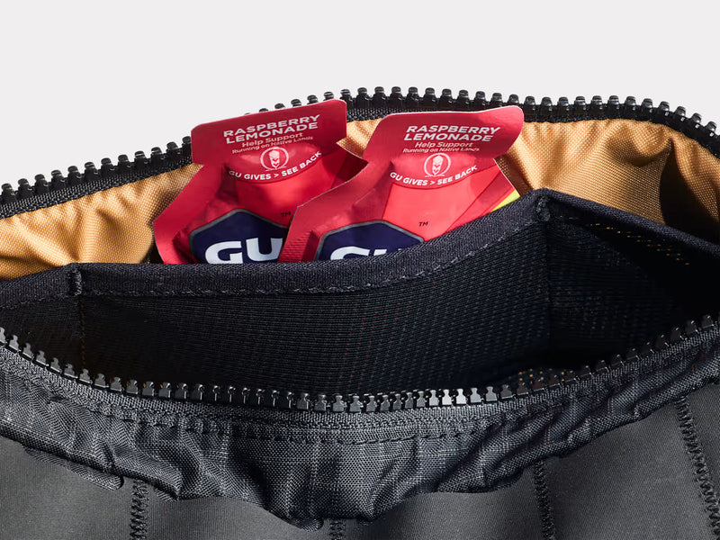 Close‑up of the Trek Adventure Triangle Bag open to show zipper, beige inner lining and GU snacks peeking out.