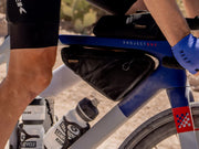 Outdoor close‑up of a cyclist riding a Trek Project One bike with two black Trek frame bags mounted above the bar and another mounted below the bar.