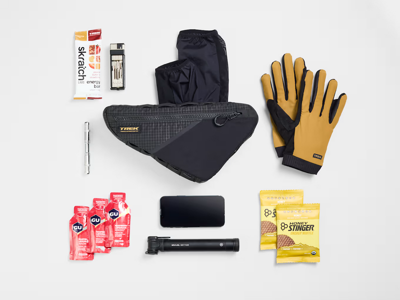 Flat lay of cycling gear arranged beside the Trek Adventure Triangle Bag 1.3L to illustrate its storage capacity.