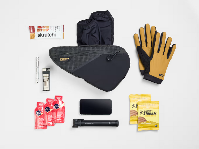 Flat lay of the Trek Adventure Triangle Bag 1.6L with a variety of cycling gear that fits inside the pouch.