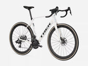 A white Trek endurance road bicycle with black components, drop handlebars, and dark wheels with beige sidewalls, photographed on a clean light gray studio background.