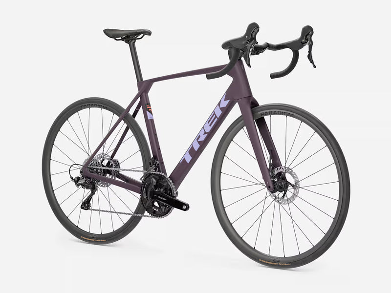 A Trek road bicycle in a dark purple frame with black components, drop handlebars, and thin tires, shown on a light gray studio background.