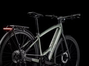 A Trek electric bicycle in a matte sage green frame with black components, shown from a side angle against a solid black background. The brand name 'TREK' is visible on the down tube.