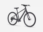 A matte black stepover cruiser electric bicycle with a step-through frame, front suspension fork, and integrated rear rack, shown from a three-quarters front angle on a light gray studio background.