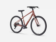 A Trek cruiser bicycle in a matte reddish-brown frame with black components, shown from a three-quarter angle on a light gray studio background.