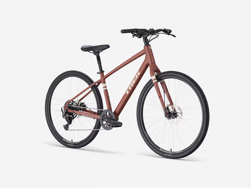A Trek cruiser bicycle in a matte reddish-brown frame with black components, shown from a three-quarter angle on a light gray studio background.