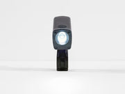 A black tactical LED bike light with its front light illuminated, standing vertically on a white surface against a white background.