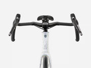 Close-up front view of a bicycle handlebar area showing black drop handlebars, black saddle, and a white frame with a subtle blue and gray speckled pattern and a small logo near the top tube.