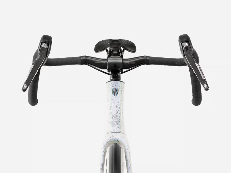 Close-up front view of a bicycle handlebar area showing black drop handlebars, black saddle, and a white frame with a subtle blue and gray speckled pattern and a small logo near the top tube.