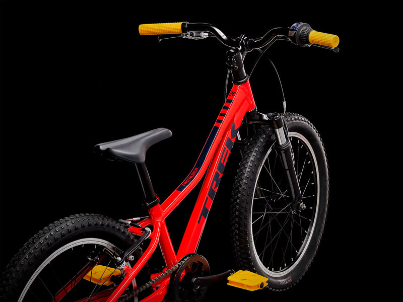 Red children's bicycle with black frame and yellow handlebar grips on a black background