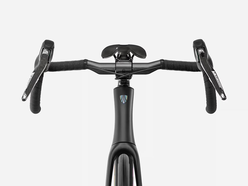 Close-up front view of ablack road endurance bicycle handlebar setup with drop handlebars, black saddle, and a small blue-and-white shield logo on the frame, shown on a light gray background.