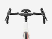 Close-up front view of a drop-bar endurance road bicycle handlebar setup with black grips, black saddle and handlebar components, mounted on a white bicycle frame against a light gray studio background.