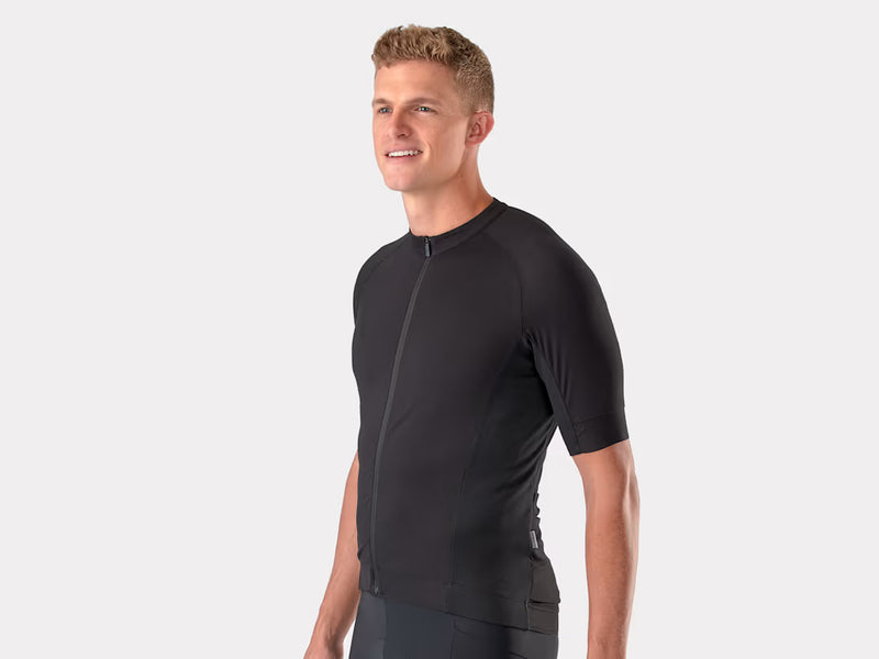 A man wearing a black short-sleeve cycling jersey with a full front zipper, shown from the waist up against a light gray studio background.