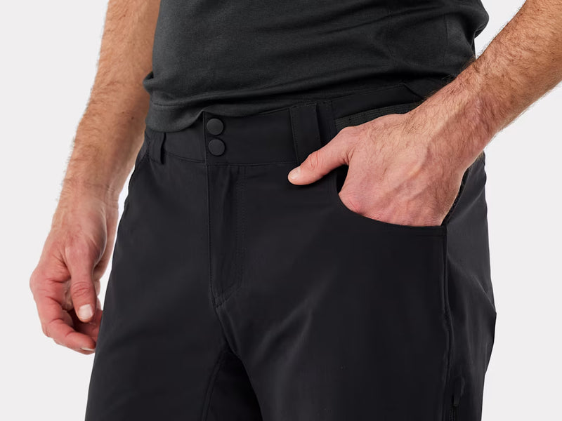 Close-up of a person wearing mtb black athletic shorts with a side pocket and two front buttons, paired with a dark gray shirt against a light gray background.
