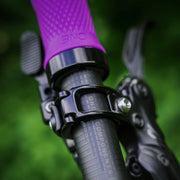 Close-up of a bicycle handlebar with purple grip and black components against a green blurred background