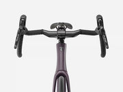 Front view of a road bicycle handlebar area showing a matte dark purple frame, black drop handlebars, black brake levers with Shimano branding, and a black saddle against a light gray background.