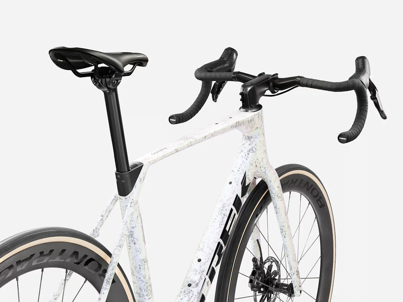 Close-up of a road bicycle frame and handlebars, showing a white frame with a subtle light gray speckled pattern, black saddle and handlebar tape, and black wheels against a light gray background.