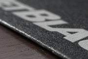 Close‑up of the JetBlack Trainer Mat on hardwood flooring showing the durable rubber texture and sealed edge.