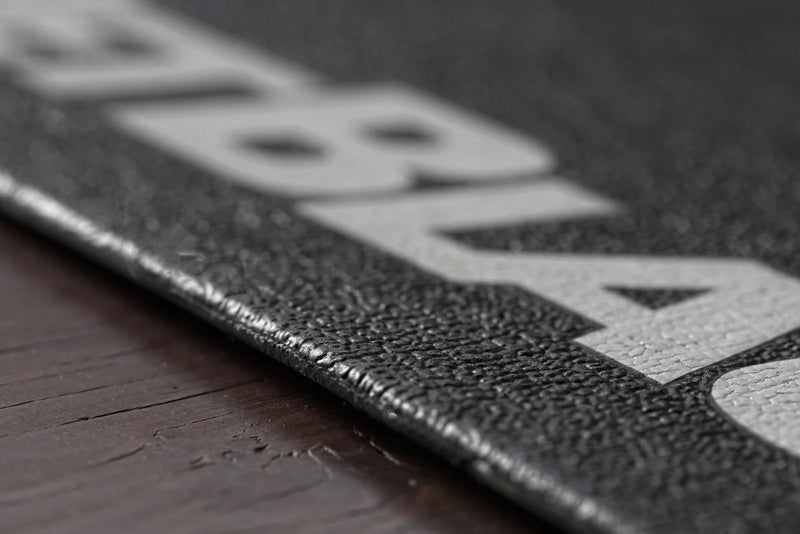 Close‑up of the JetBlack Trainer Mat on hardwood flooring showing the durable rubber texture and sealed edge.