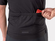 Close-up of a black athletic jersey with a side pocket being filled with a red packet by a person's hand, on a light gray background.