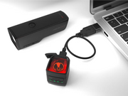 Black electronic device with red light on a white surface next to a laptop.