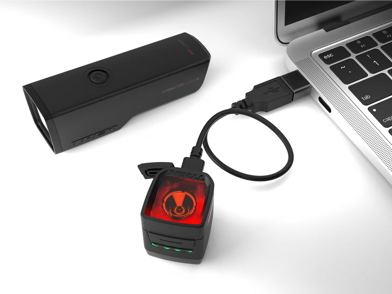 Black electronic device with red light on a white surface next to a laptop.