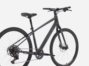 A matte black Trek bicycle with a step-through frame, front suspension fork, disc brakes, and a rear derailleur, shown from a side angle against a light gray background.