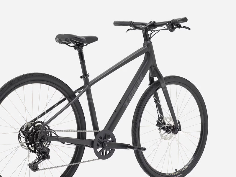 A matte black Trek bicycle with a step-through frame, front suspension fork, disc brakes, and a rear derailleur, shown from a side angle against a light gray background.
