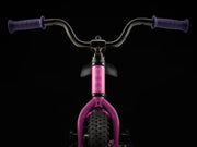 Pink balance bike with black handlebars on a black background