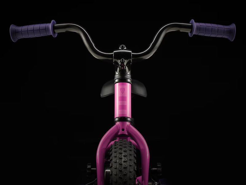 Pink balance bike with black handlebars on a black background