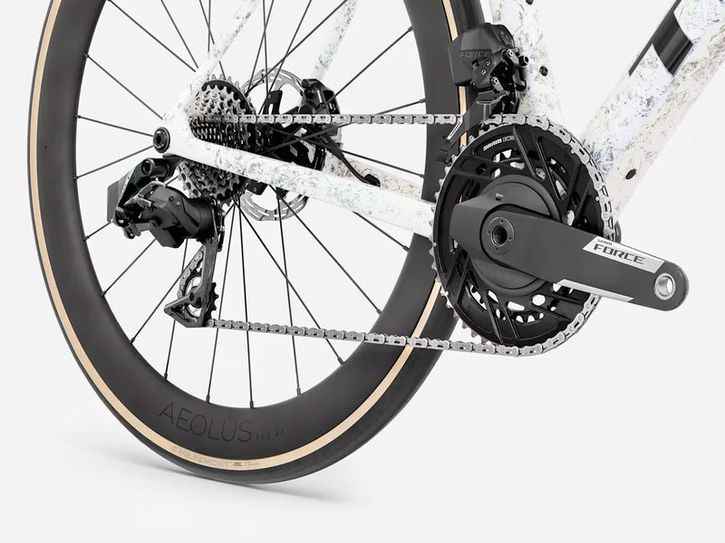 Close-up of a bicycle's rear wheel, chainring, crankset, and derailleur on a light gray studio background. The wheel is black with a beige tire wall, and the crankset is dark gray/black with a visible 'FORCE' brand mark.