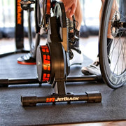 Lifestyle image of an indoor personal gym with a trainer setup positioned on top of the JetBlack Trainer Mat.