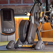 Lifestyle image of an indoor trainer setup with JetBlack Freedom Rocker Feet installed underneath the trainer.