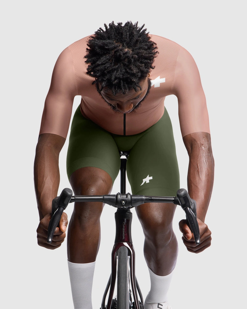 Person wearing green cycling shorts with a logo, riding a stationary bike against a plain background