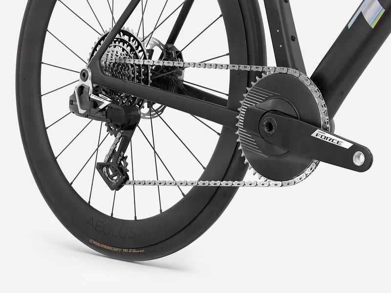 Close-up of a black endurance road bicycle drivetrain showing the rear wheel, chainring, chain, cassette, and crankset with a visible Force brand mark on the arm.