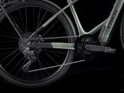 Close-up of a Trek hybrid electric bicycle showing the rear wheel, chainring, cassette, chain, and part of the frame against a black background.