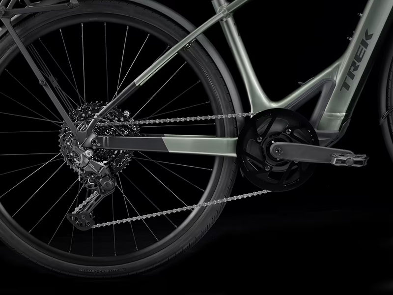 Close-up of a Trek hybrid electric bicycle showing the rear wheel, chainring, cassette, chain, and part of the frame against a black background.