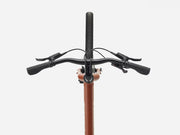 Close-up of a cruiser bicycle handlebar with black grips, brake levers, and cables, attached to a copper-colored frame against a light gray background.