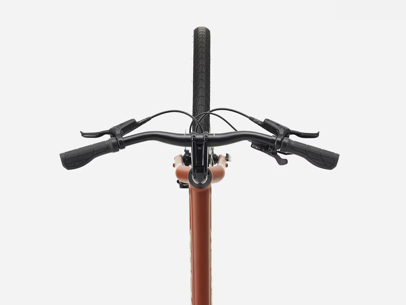 Close-up of a cruiser bicycle handlebar with black grips, brake levers, and cables, attached to a copper-colored frame against a light gray background.