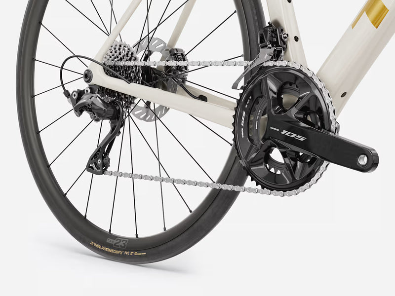 Close-up of a bicycle's rear wheel and drivetrain, showing a black disc wheel, rear derailleur, chainring, cassette, and chain, with part of a cream-colored frame visible.