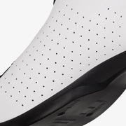 Close-up of a white sneaker with black perforations on a light gray background