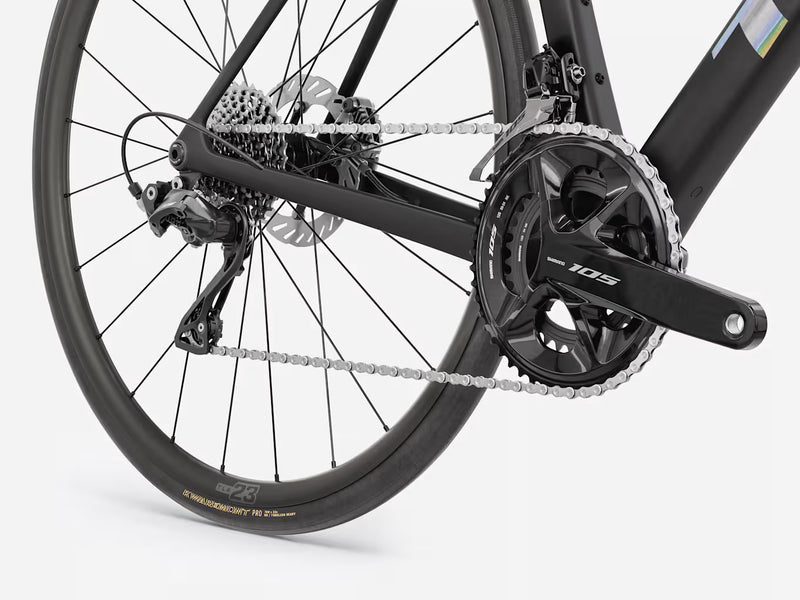 Close-up of a black road bicycle rear wheel and drivetrain, showing the chainring, chain, cassette, rear derailleur, and disc brake on a light gray studio background.