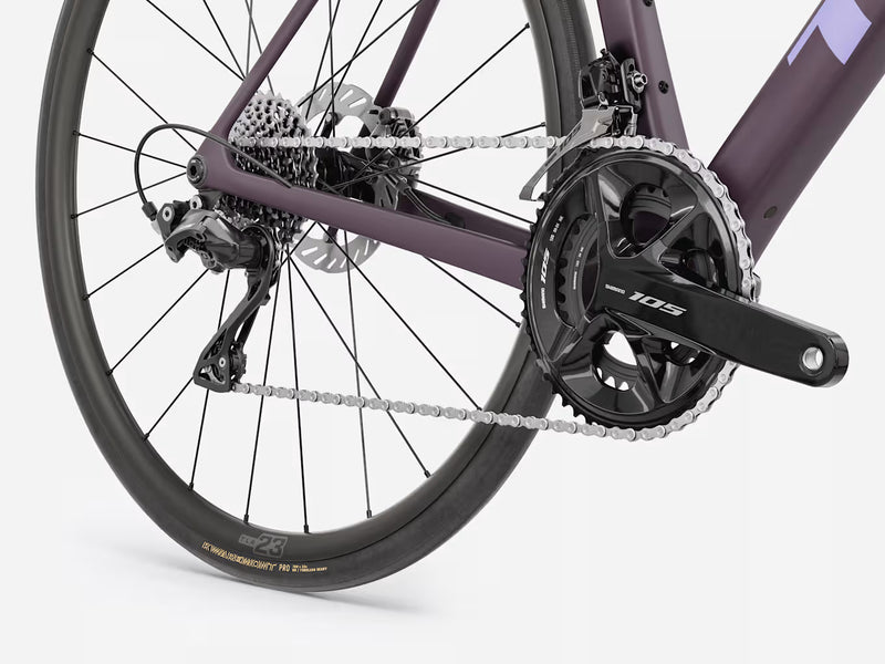 Close-up rear section of a road bicycle showing the dark purple frame, black drivetrain components, chainring, cassette, rear wheel, and disc brake on a light gray studio background.