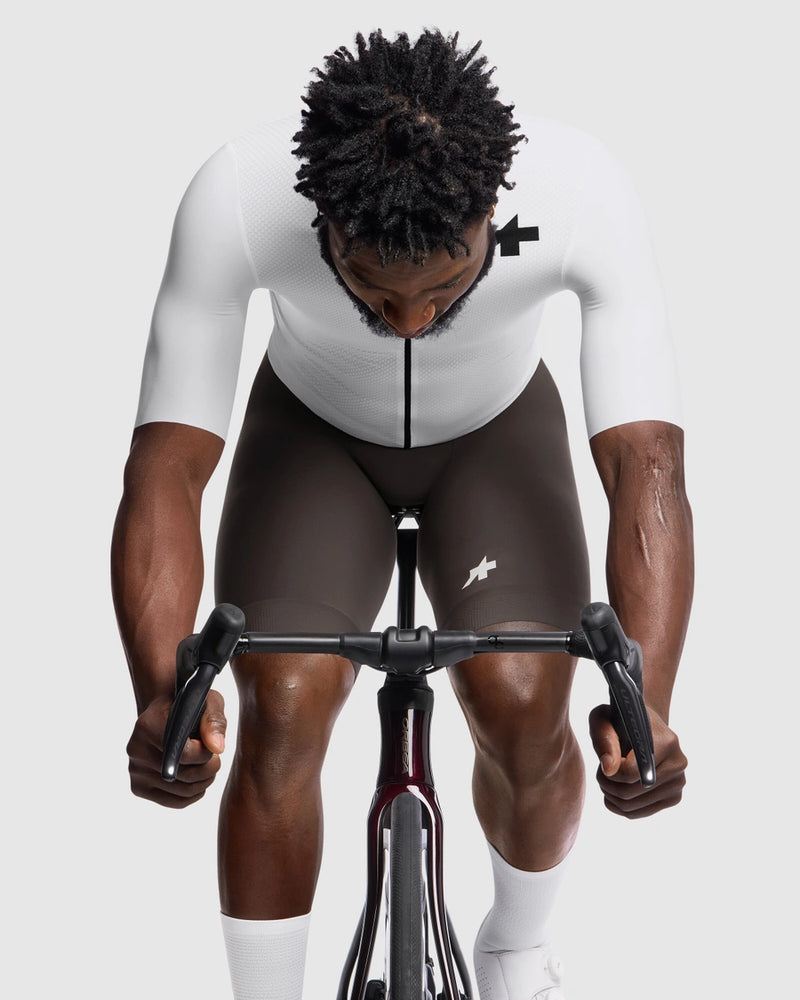 Person wearing a white cycling outfit and brown shorts on a white background