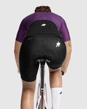 Person wearing black cycling shorts and a purple top on a white background