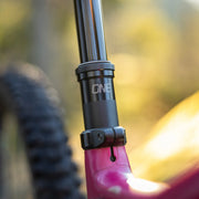 Close-up of a bicycle suspension fork with 'ONE' branding against a blurred natural background.