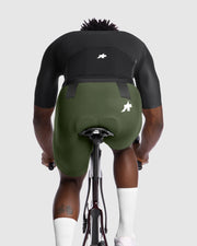 Person wearing a black cycling jersey and green bib shorts with a brand logo on a white background