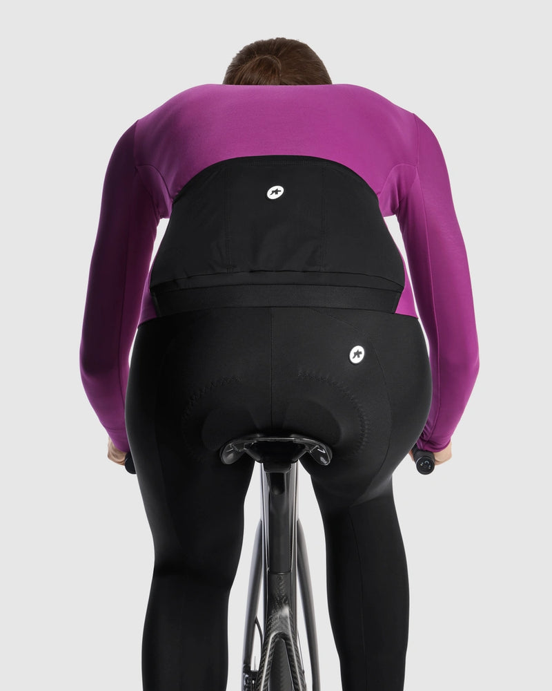 Female cyclist wearing the Assos UMA GT Spring Fall LS Jersey C2 in Purple Alchemy, rear view on a road bike showing the black rear pockets and central ASSOS logo