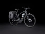 A matte black electric bicycle with a rear pannier bag and a white water bottle mounted on the frame, photographed against a solid black studio background.