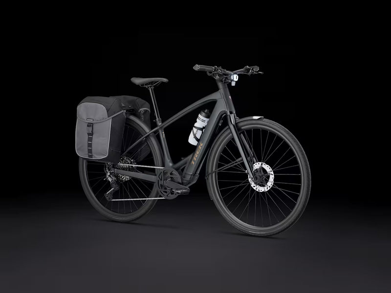 A matte black electric bicycle with a rear pannier bag and a white water bottle mounted on the frame, photographed against a solid black studio background.